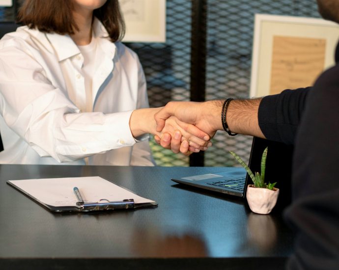 a man and a woman shaking hands in front of a laptop